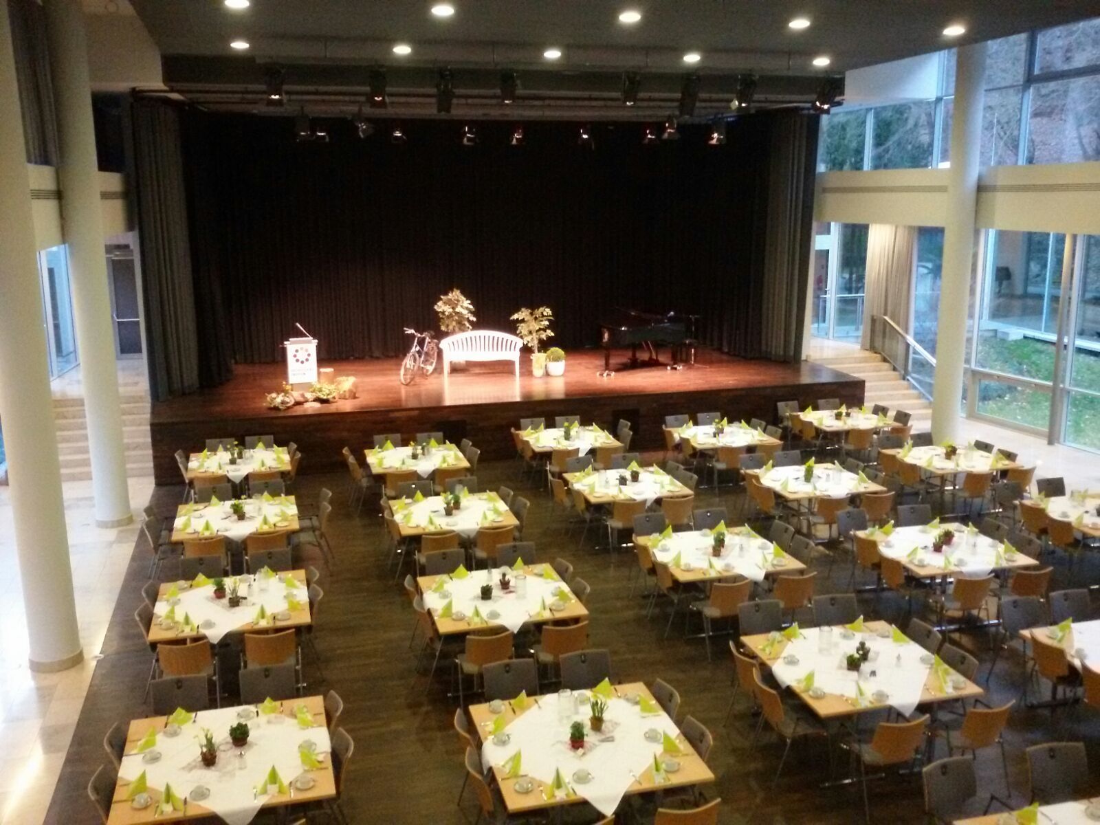 Blick in den Quellensaal mit Bühne und Tischen vor der Bühne.