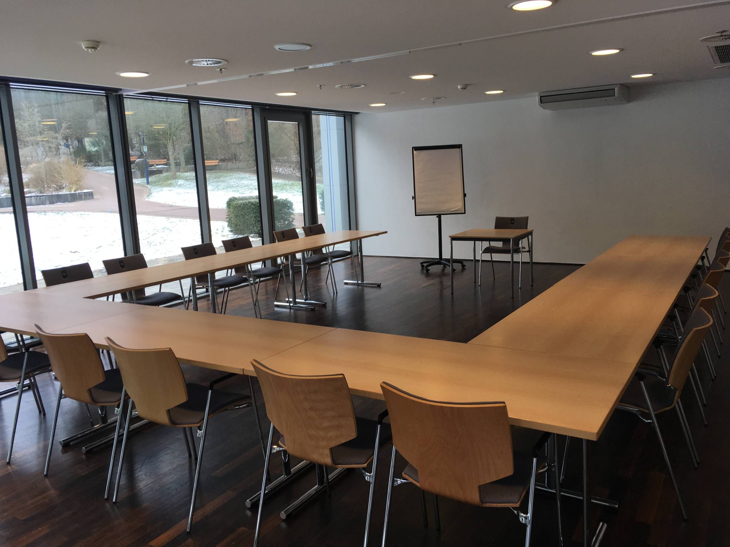 Blick in einen Seminarraum der Wandelhalle Bad Wildungen. Tische und Stühle sind in U-Form gestellt. Davor ist ein Flipchart und ein kleiner Tisch mit Stuhl zu sehen.