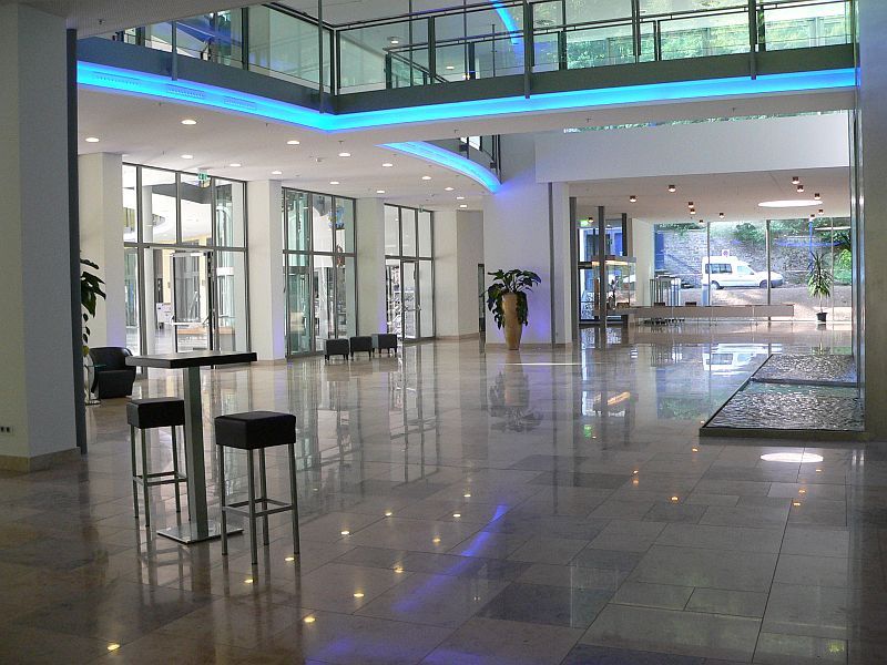 Blick in das Foyer der Wandelhalle Bad Wildungen. Rechts im Bild ist ein teil der Wasserwand zu sehen. Links der Eingangsbereich. Oben im Bild sind die Brücke und die Empore aus dem 1. Obergeschoss zu sehen.