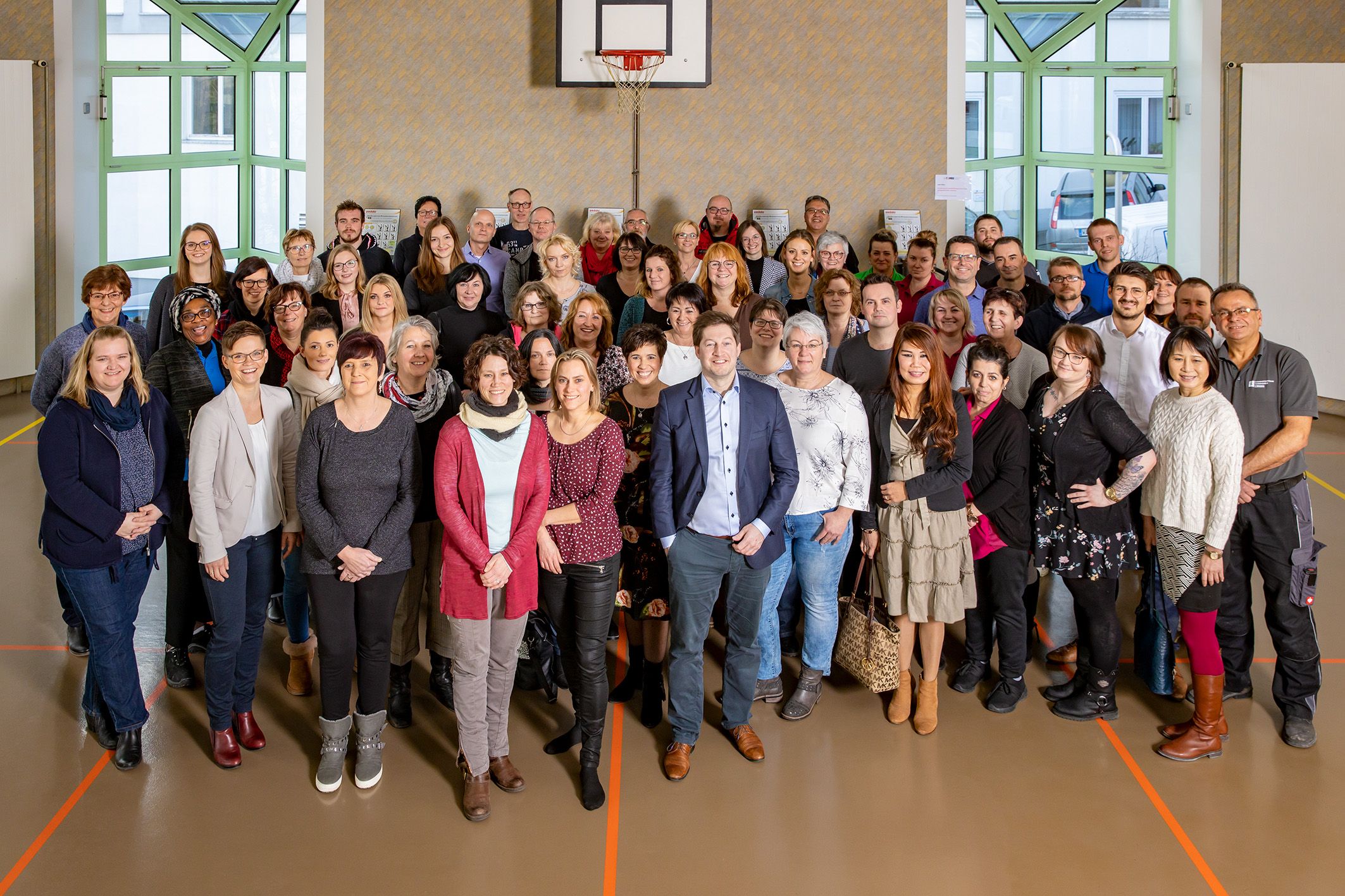 Teamfoto der Mitarbeiter des Gesundheitzentrums Helenenquelle. Die Menschen stehen in einer Turnhalle unter einem Basketballkorb.