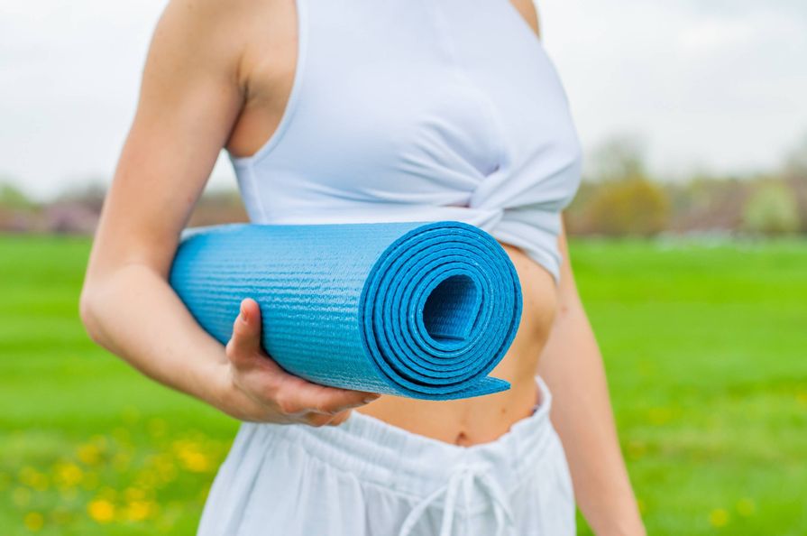 Titelbild des Yogasommers in Bad Wildungen. Es ist nur ein Teil des Oberkörpers einer Frau zu sehen, die eine blaue aufgerollte Yogamatte in der Hand hält.