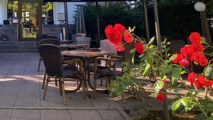 Eine Terrasse mit braunen Tischen und Stühlen und im Vordergrund schöne rote Blumen