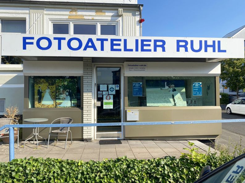 Außenansicht des Eingangs des Fotoateliers Ruhl Links neben dem Eingang stehen zwei Stühle und ein Tisch. Im Schaufenster sind drei Hochzeitsbilder zu sehen.