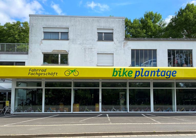 Außenansicht des Fahrradgeschäfts bikeplantage. Zu sehen ist eine Fensterfront hinter der Fahrräder stehen sowie die leeren Parkplätze vor dem Geschäft.