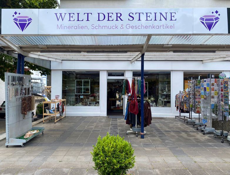 Außenansicht des Eingangs des Geschäfts Welt der Steine - Minderalien, Schmuck und Geschenkartikel. Vor dem Eingang sind Ständer mit Tüchern, Schmuck und Ansichtskarten zu sehen.
