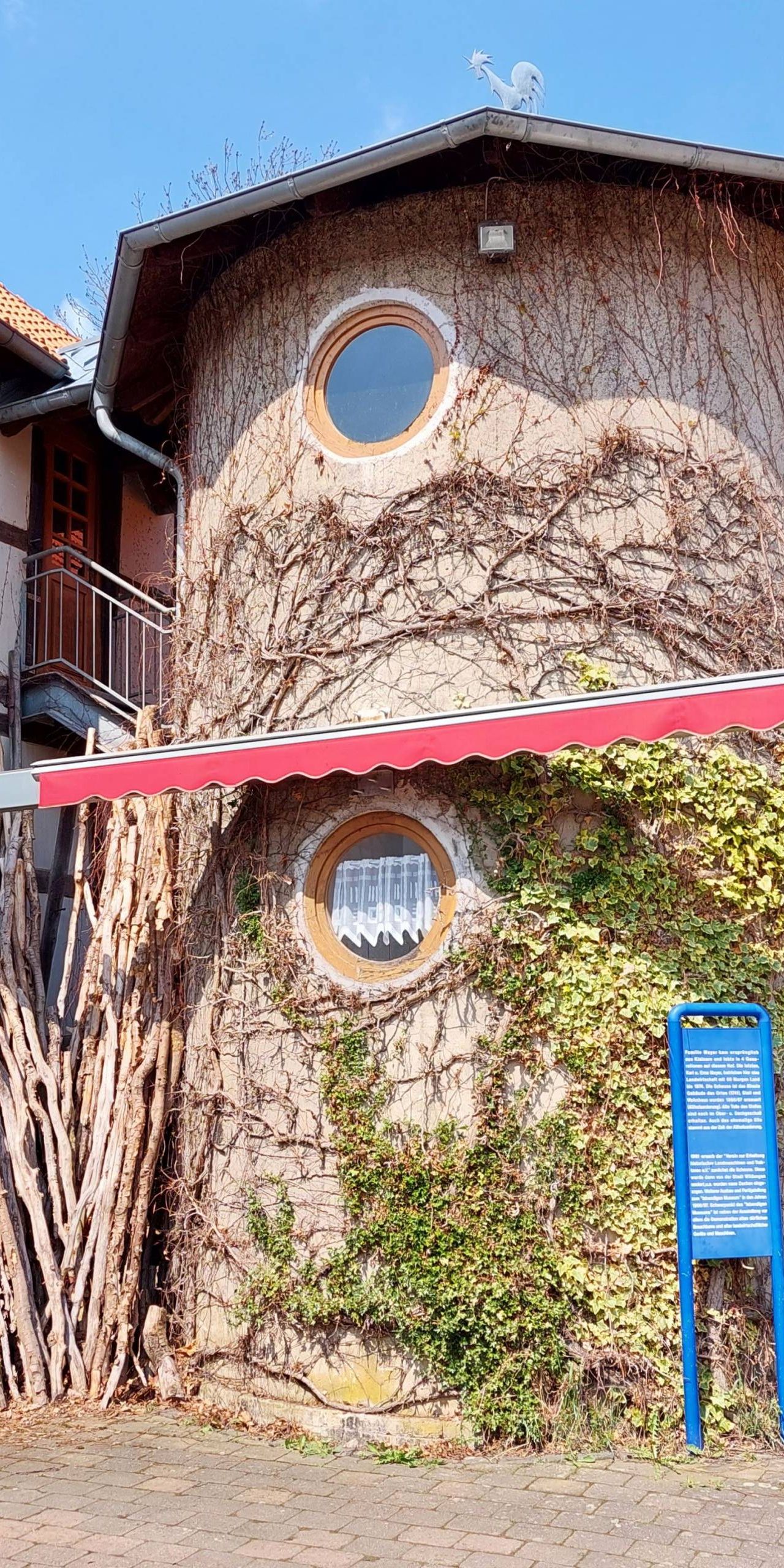 Zu sehen ist das Lebendige Museum in Odershausen. Der mittige Teil des Gebäudes sieht aus wie ein Baumstamm. Links sieht man ein weiß braunes Fachwerkhaus. Auf der rechten Seite des Bildes sieht man ein Haus aus Holz.