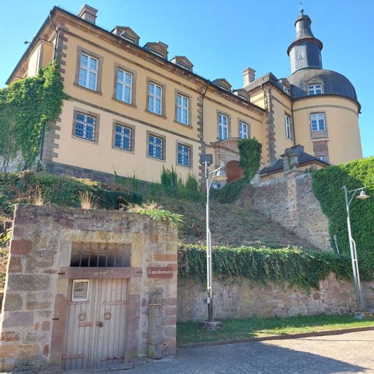 Nahaufnahme des Lapidariums unter dem Schloss Friedrichstein. Im Vordergrund ist unten links das Lapidarium zu sehen. Im Hintergrund ist Schloss Friedrichstein zu sehen.