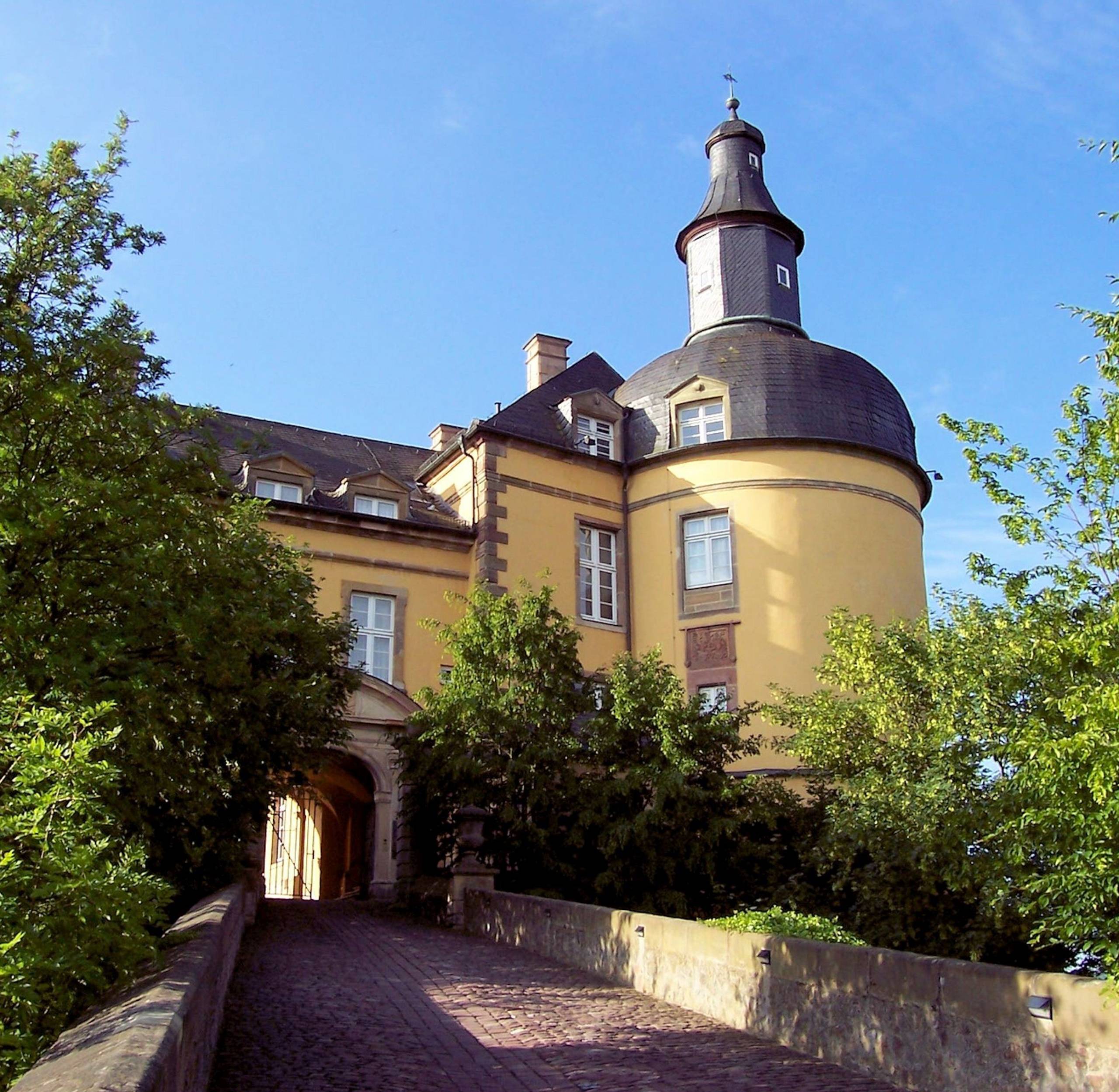 Nahaufnahme von Schloss Friedrichstein. Im Vordergrund ist der Weg zum Tor des Schlosses zu sehen mit Bäumen links und rechts.