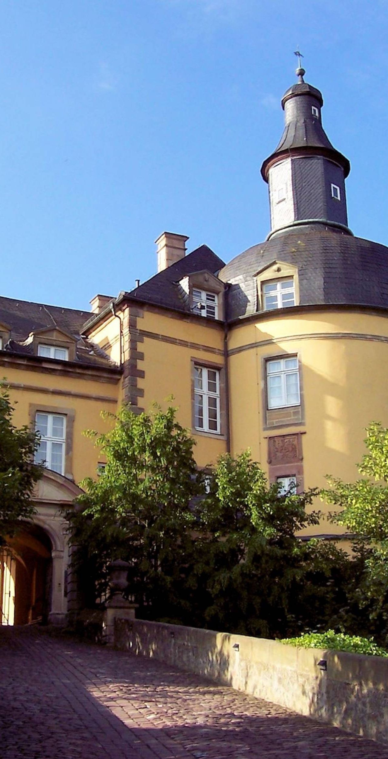 Nahaufnahme von Schloss Friedrichstein. Im Vordergrund ist der Weg zum Tor des Schlosses zu sehen mit Bäumen links und rechts.