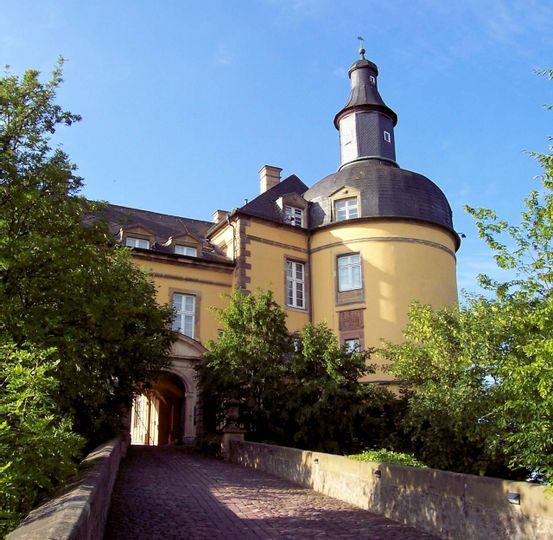 Nahaufnahme von Schloss Friedrichstein. Im Vordergrund ist der Weg zum Tor des Schlosses zu sehen mit Bäumen links und rechts.