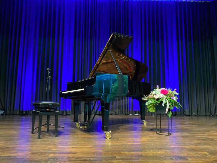 Schwarzes Klavier auf der Bühne in der Wandelhalle. Im Hintergrund ein blauer Vorhang. Rechts vom lavier steht ein Blumenstrauß.