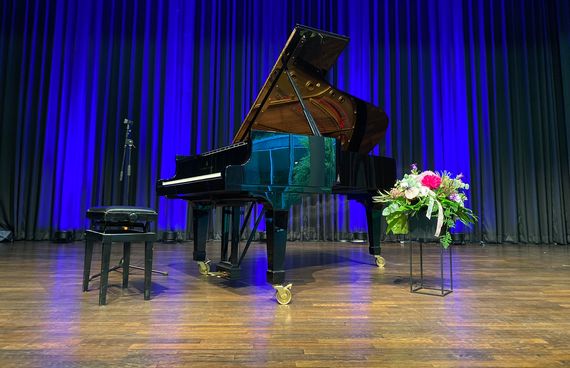 Schwarzes Klavier auf der Bühne in der Wandelhalle. Im Hintergrund ein blauer Vorhang. Rechts vom lavier steht ein Blumenstrauß.