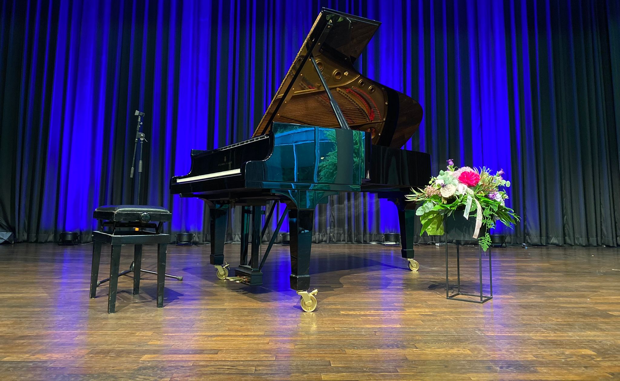Schwarzes Klavier auf der Bühne in der Wandelhalle. Im Hintergrund ein blauer Vorhang. Rechts vom lavier steht ein Blumenstrauß.