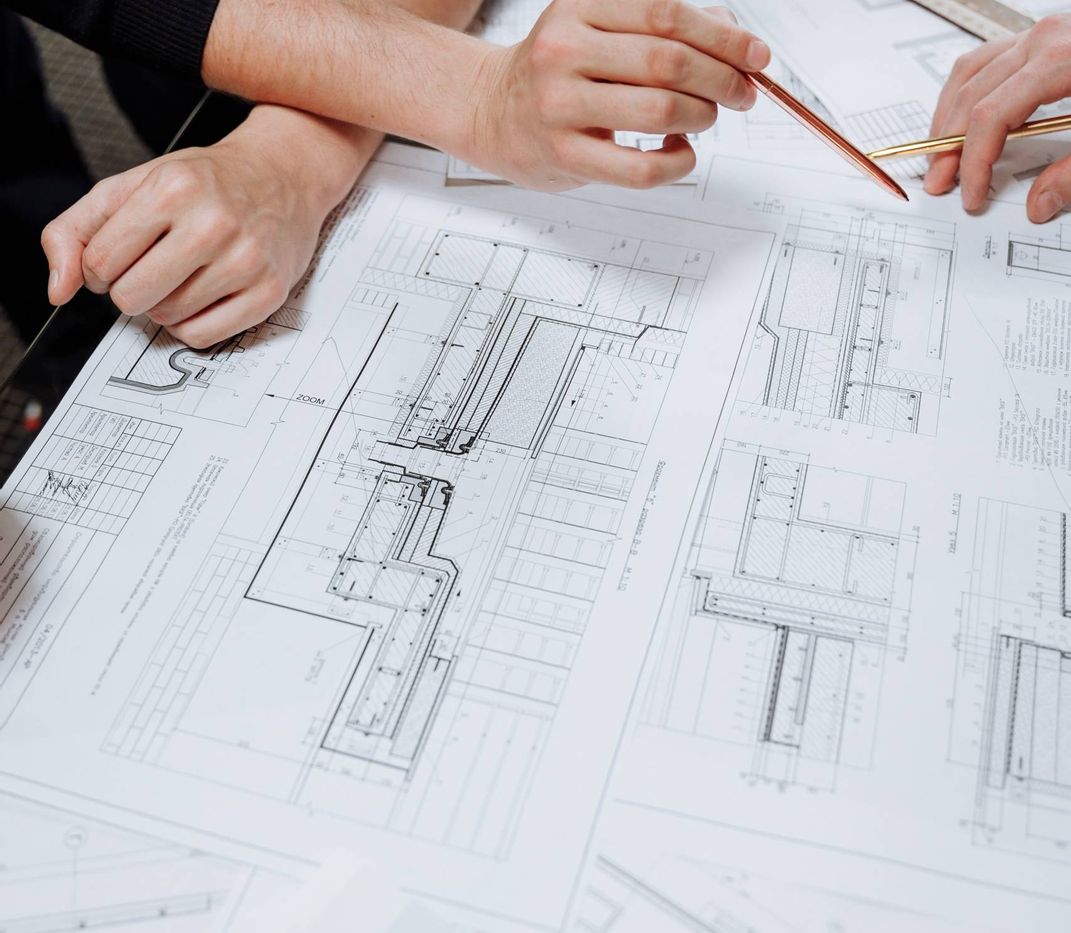 2 Personen arbeiten mit Stiften an einem Bauplan.