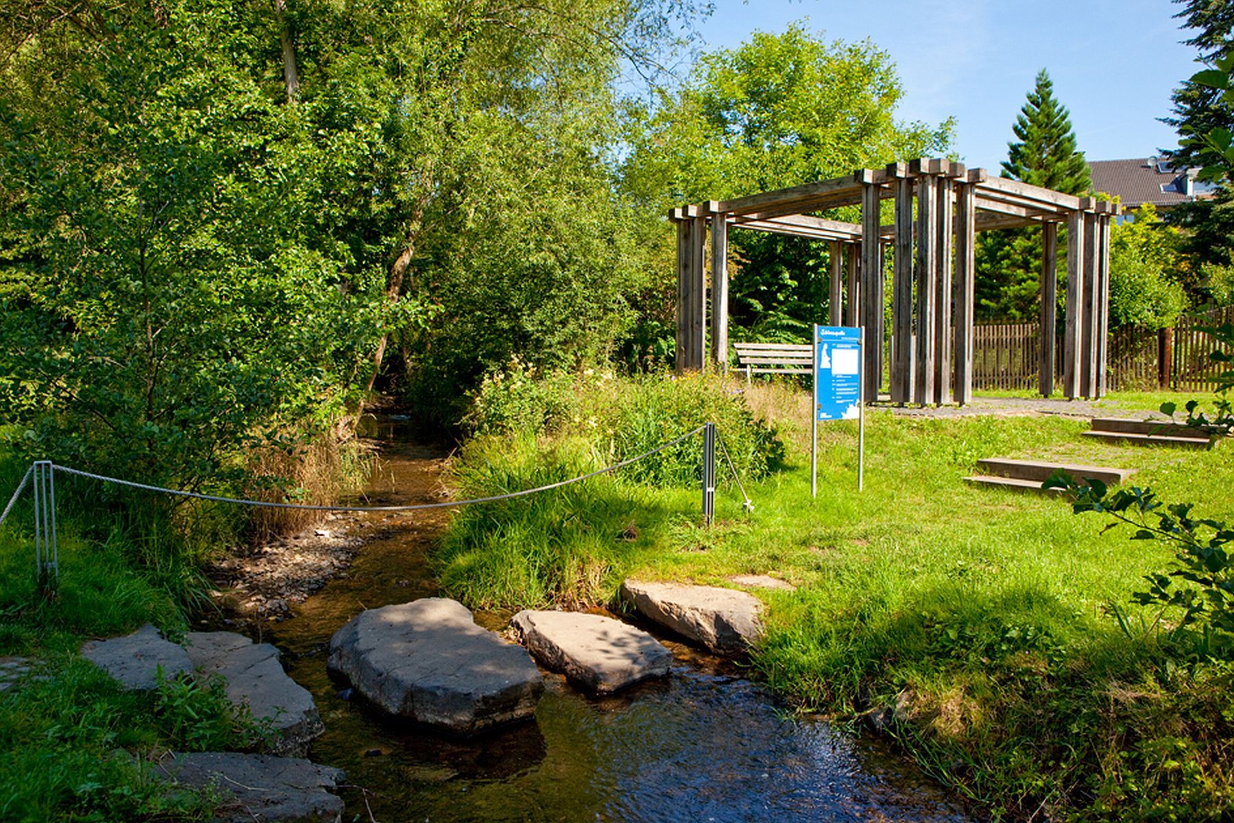 Blick auf die Bad Wildunger Schlossquelle mit grüner Wiese und einem vorbei fließenden Bach