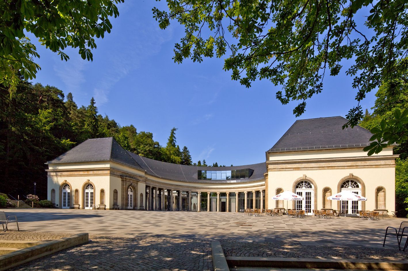 Wandelhalle Bad Wildungen bei blauem Himmel umgeben von grünen Bäumen.