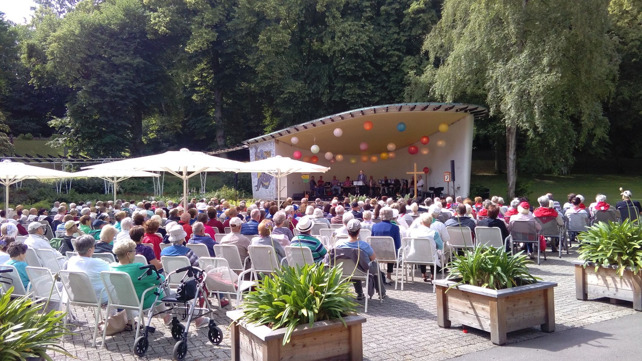 Blick auf den Musikpavillon im Kurpark Bad Wildungen. Viele Menschen sitzen auf Stühlen davor und schauen sich ein Konzert an.