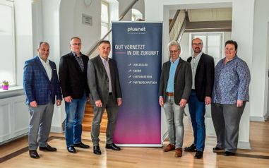 6 Personen stehen im Rathaus neben einem blau-pinken Banner mit der Aufschrift "plusnet Gut vernetzt in die Zukunft".