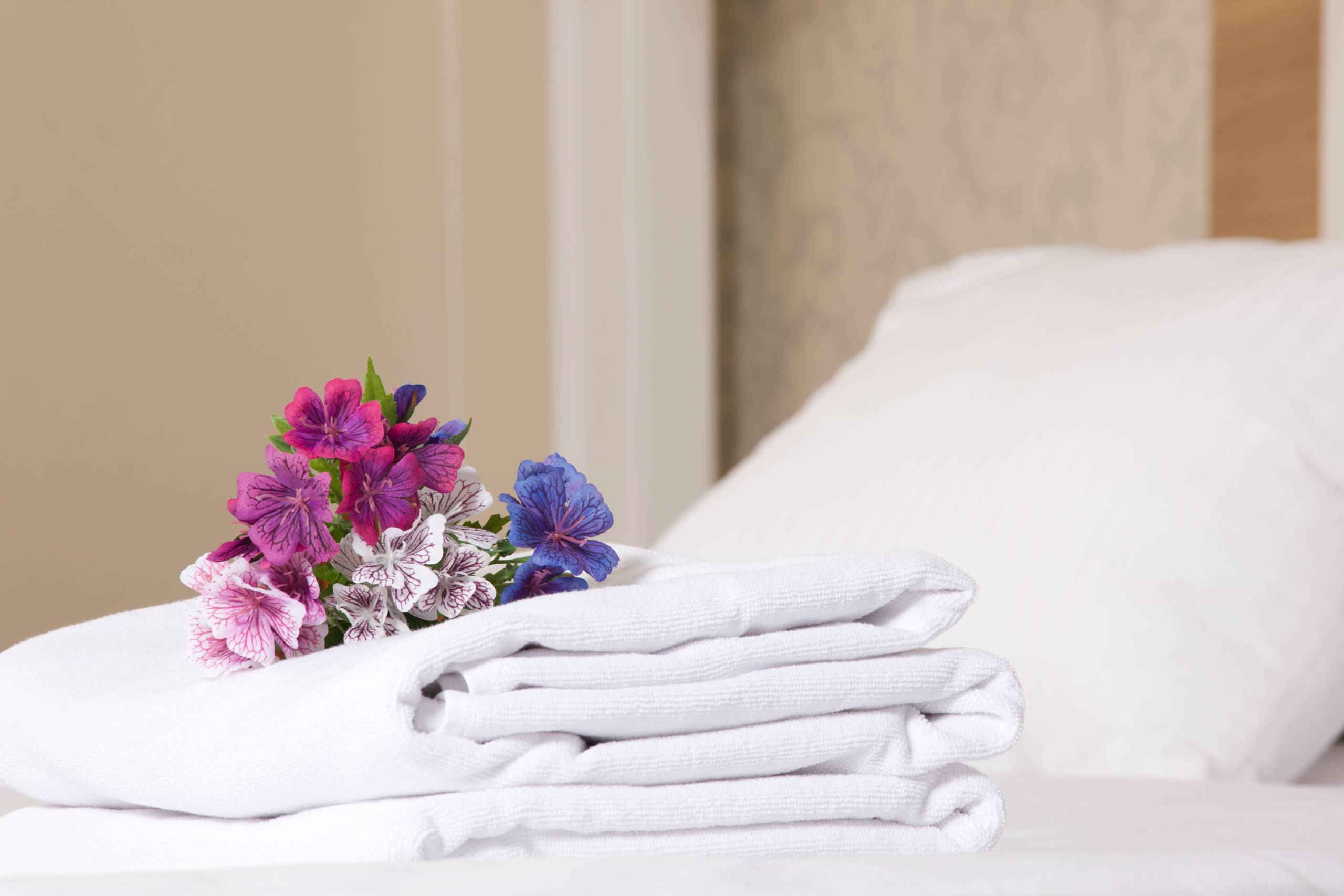 Ein Stapel Handtücher auf einem Bett. Auf den Handtüchern liegt ein Blumenstrauß.