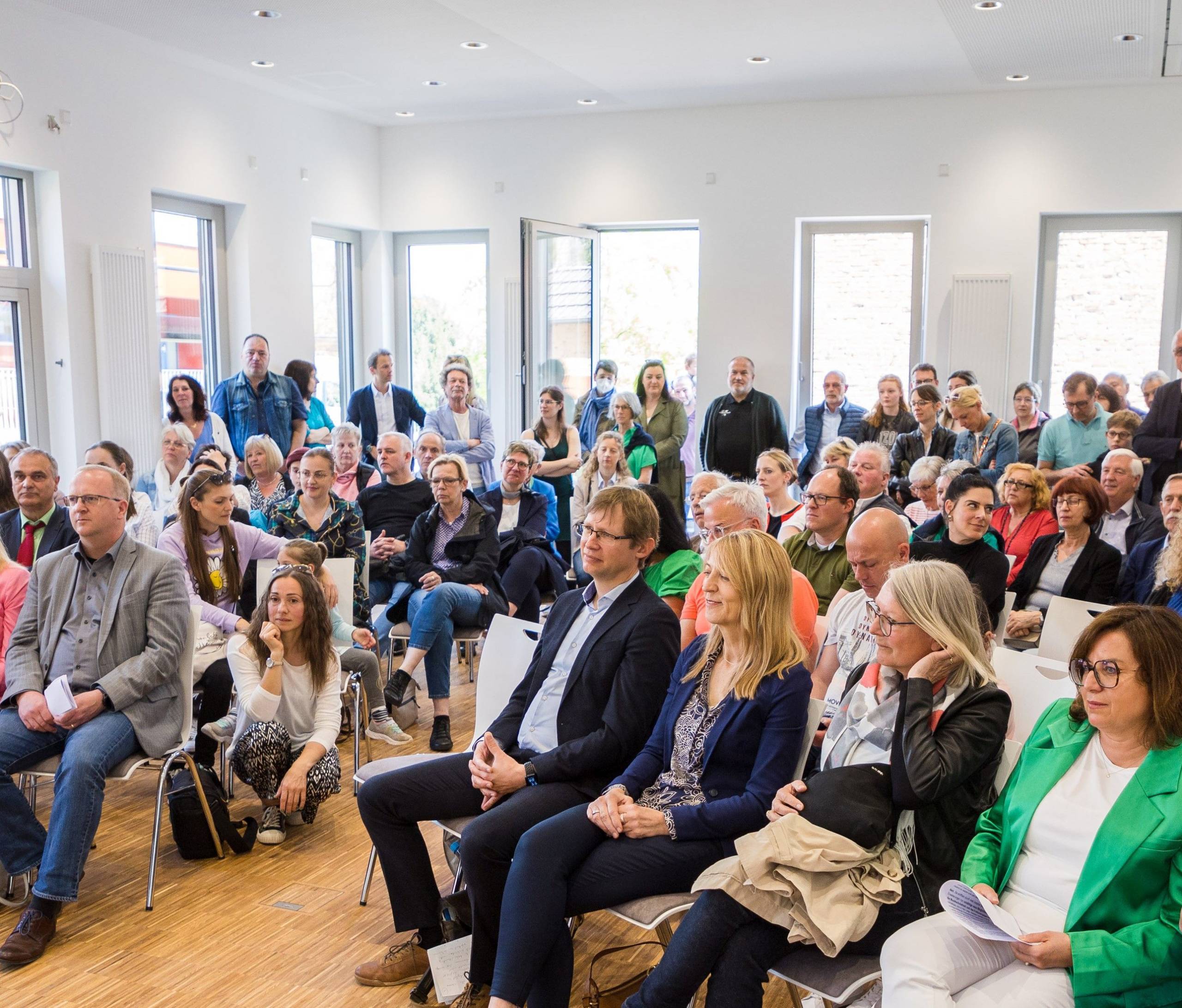 Viele Personen die in einem Raum sitzen oder stehen und nach vorne schauen
