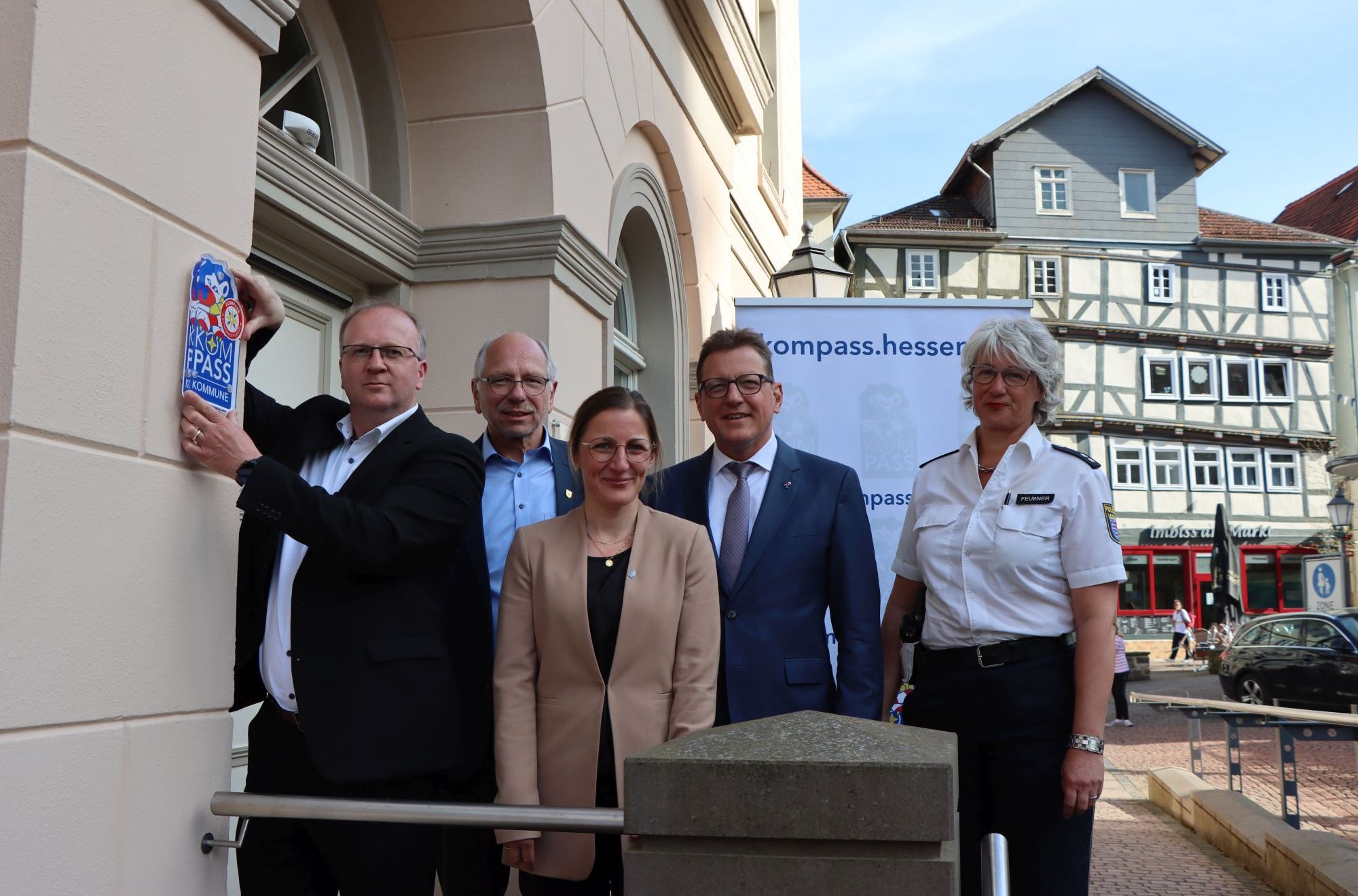5 Personen stehen am Eingang des Bürgerbüros. Der Bürgermeister hält das "Kompass"-Siegel rechts neben dem Eingang an der Wand