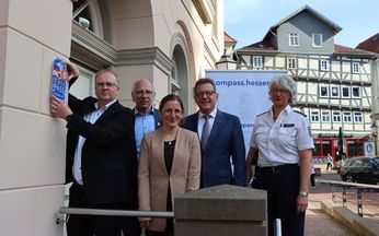 5 Personen stehen am Eingang des Bürgerbüros. Der Bürgermeister hält das "Kompass"-Siegel rechts neben dem Eingang an der Wand