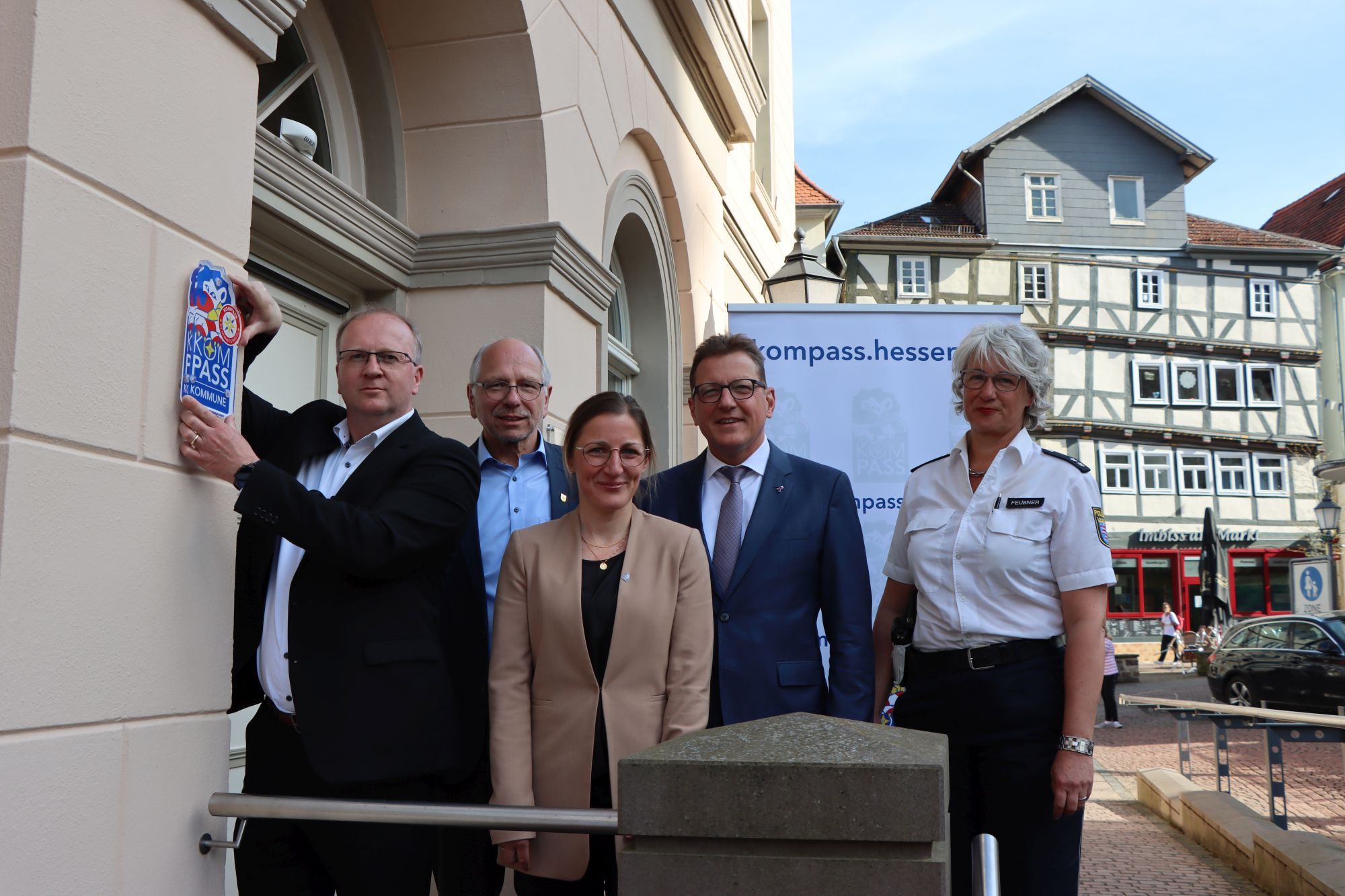 5 Personen stehen am Eingang des Bürgerbüros. Der Bürgermeister hält das "Kompass"-Siegel rechts neben dem Eingang an der Wand