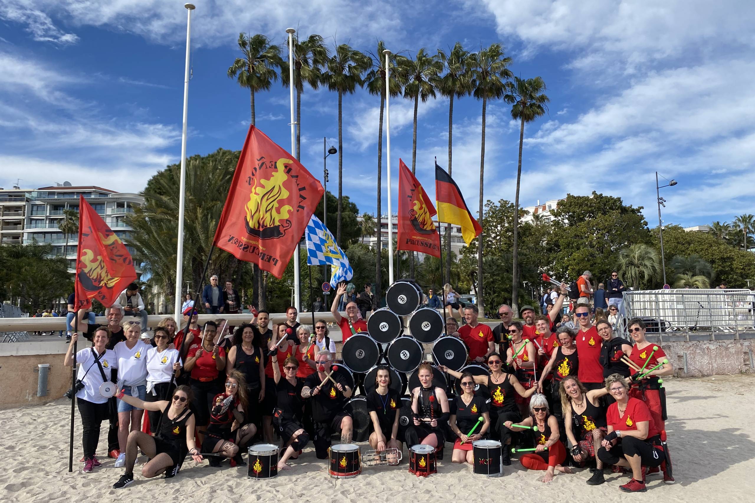 Gruppenbild der Sambagruppe Jalapeños Percussion vor Palmen und Flaggen am Strand.
