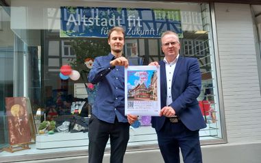 Der Bürgermeister und eine weitere Person stehen mit einem Plakat vor dem PopUp Store in der Altstadt.