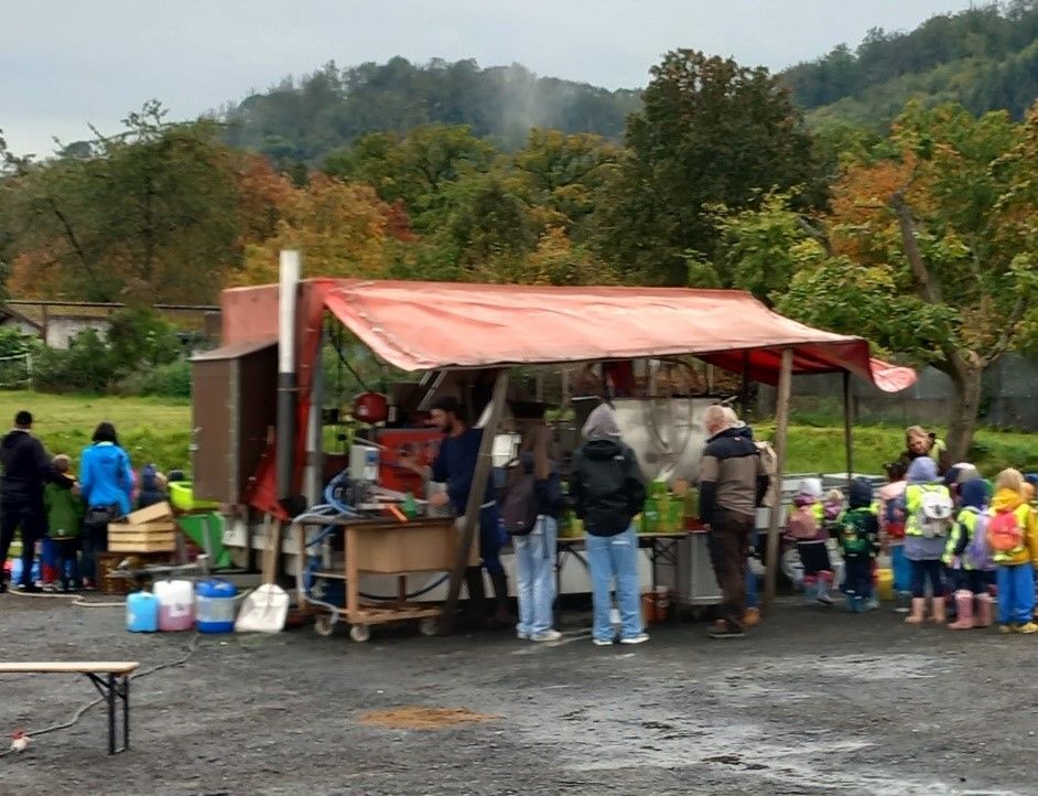 Eine Gruppe von Personen und Kindergartenkinder die an einem Säfte-Stand stehen