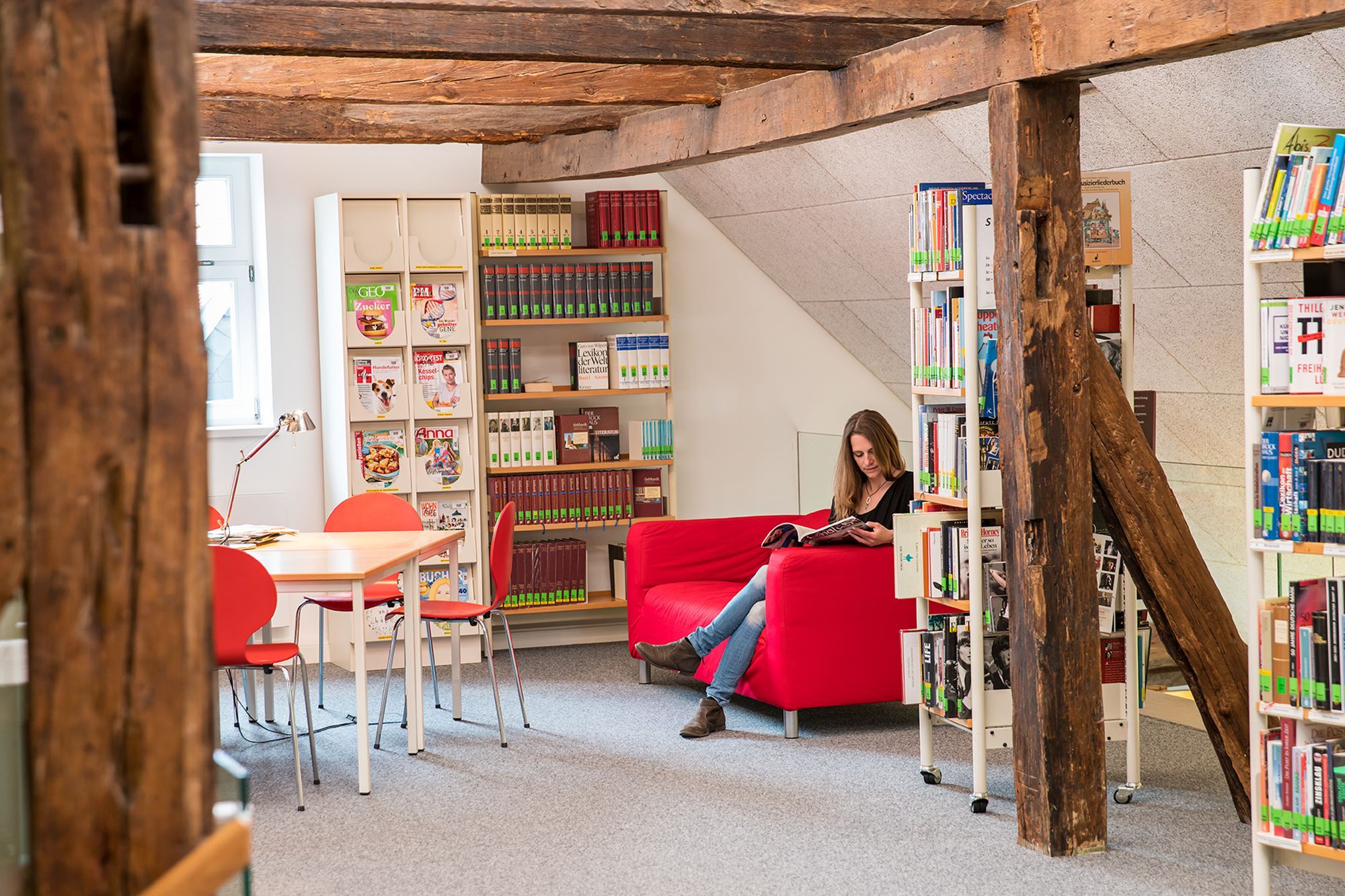 Aufnahme aus der Stadtbücherei. Eine Frau liest ein Buch auf einem Sofa zwischen Bücherregalen.