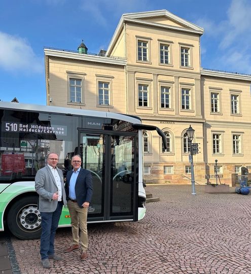 Der Bürgermeister steht mit einer anderen Person vor einem Bus mit dem Rathaus im Hintergrund