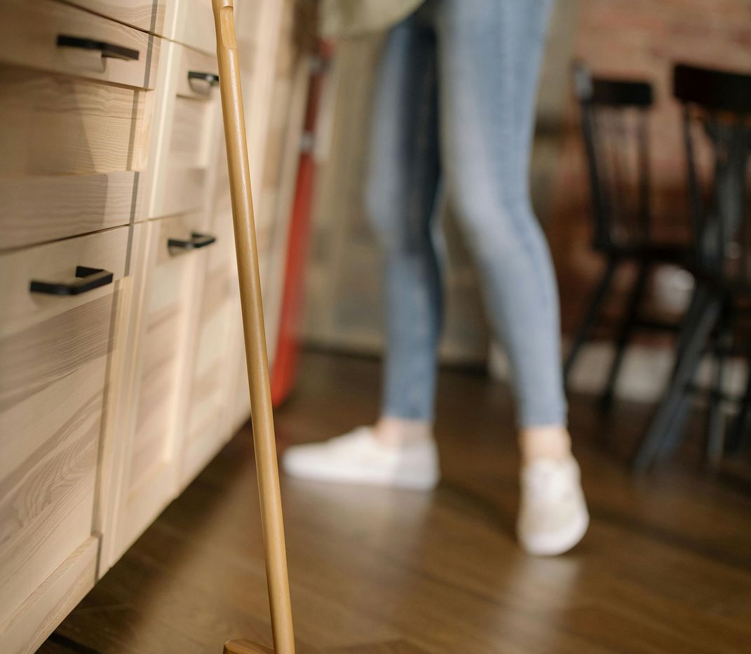 Ein Holzbesen, der an einem Unterschrank angelehnt ist.