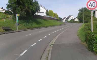 Eine Straße die Bergauf führt. Rechts und links sind Wohnhäuser von Bäumen und Büschen umgeben