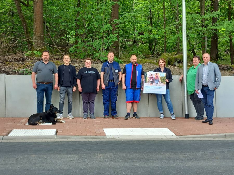 Acht Personen stehen am Straßenrand und blicken in die Kamera. Eine von ih
