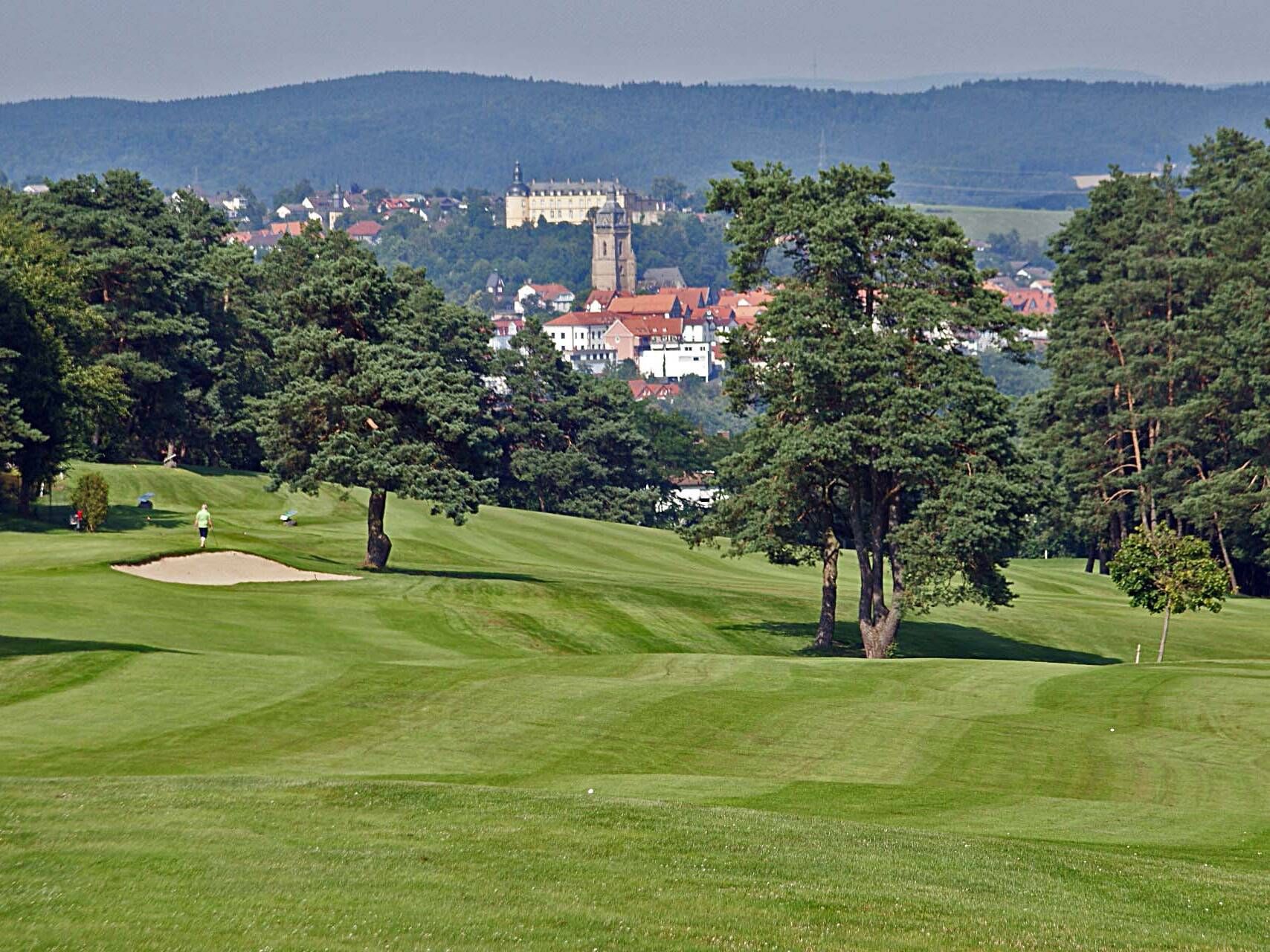 Blick aus der Ferne auf einen hügeligen Golfplatz. Im Hintergrund lässt sich die Bad Wildunger Altstadt sehen.