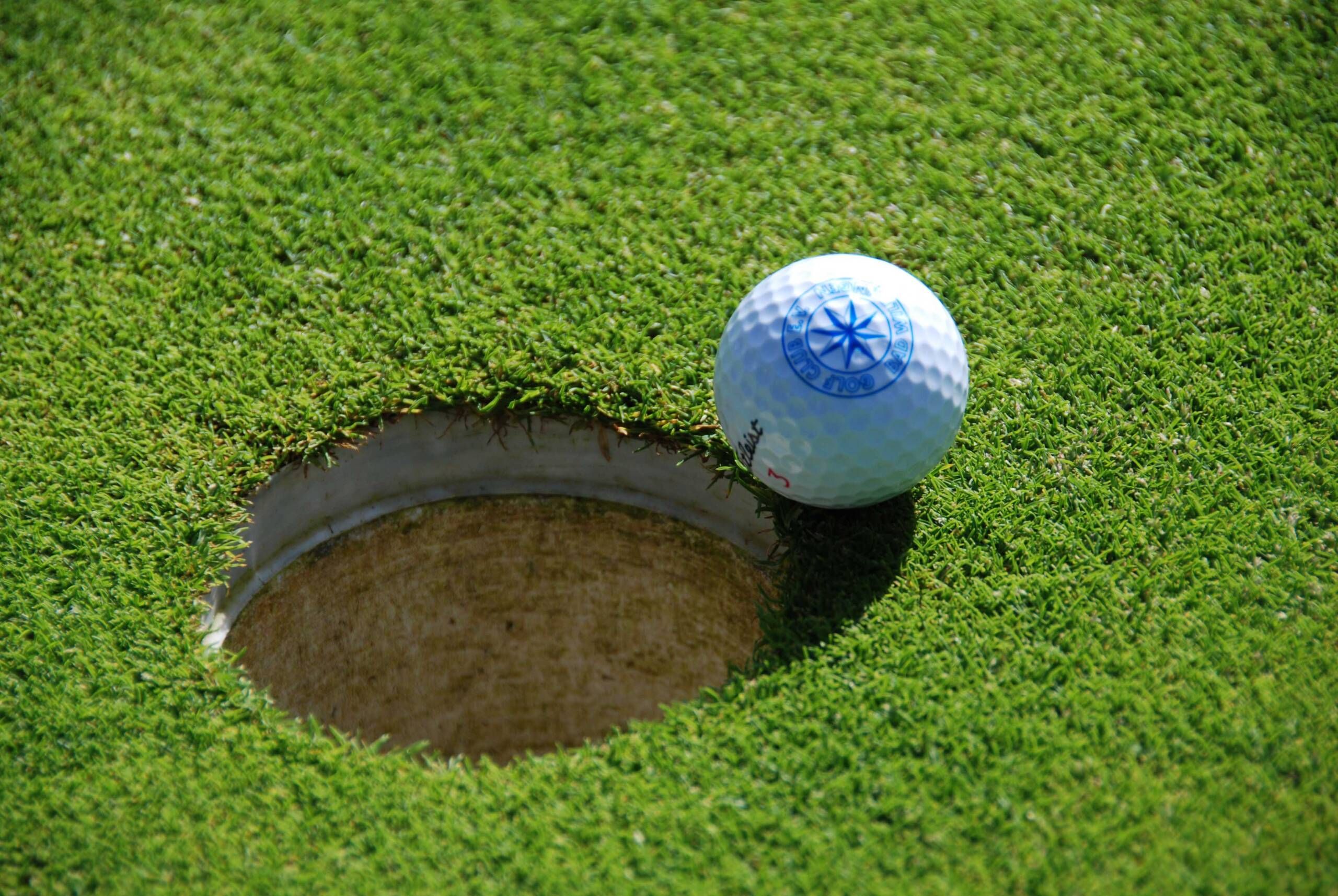 Nahaufnahme von einem Golfball, der genau am Rand des Loches liegt. Auf dem Golfball befindet sich der Waldecker Stern