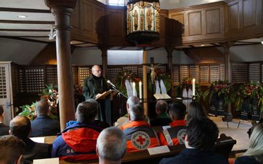 Ein Mann hält vor vielen Personen eine Rede in der Philipp-Nicolai Kirche. Um den Alter herum sind Gedenk-Kränze aufgebaut.