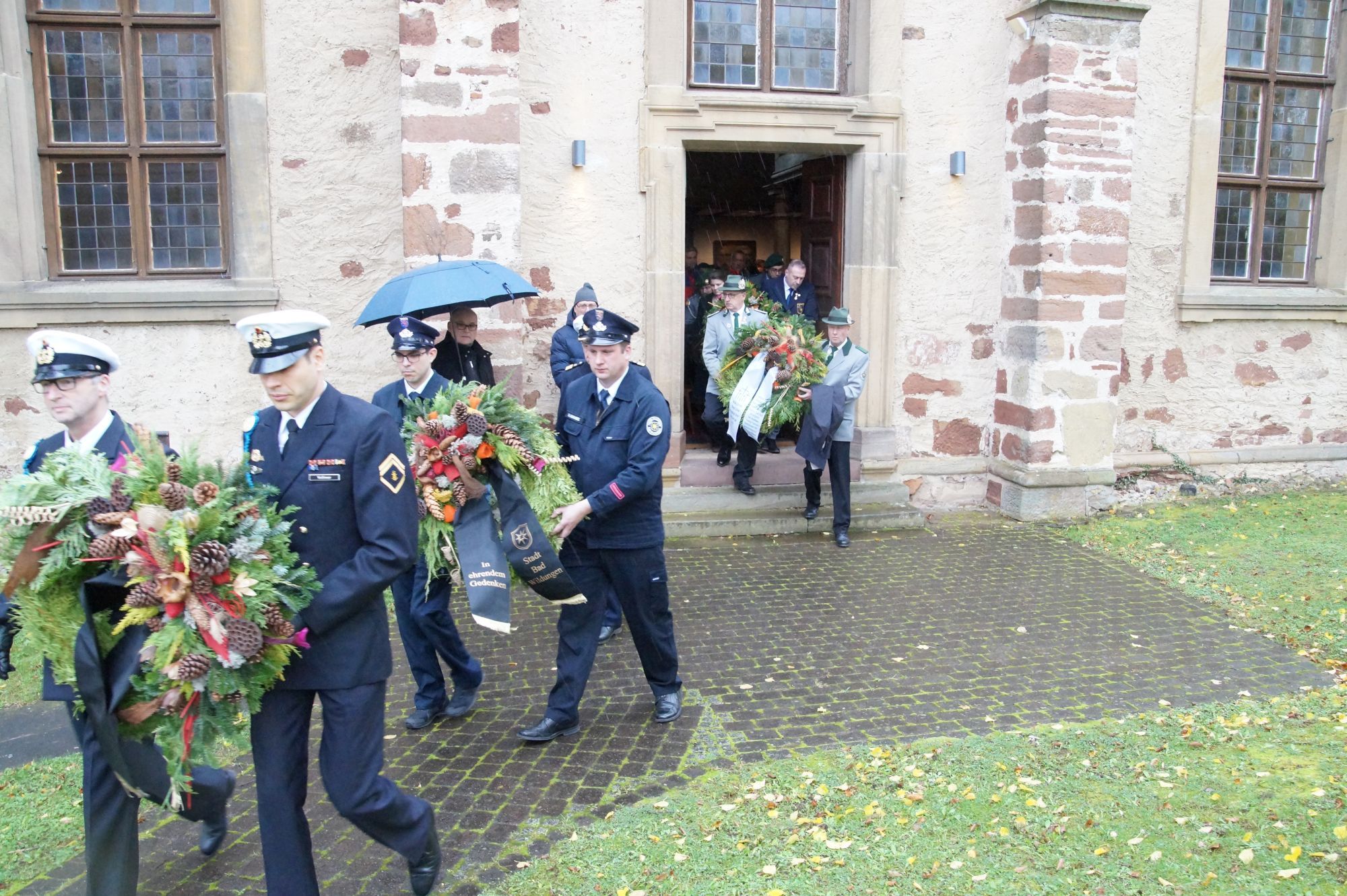 Männer in Uniformen, die mit Kränzen aus der Phillip-Nicolai Kirche gehen.
