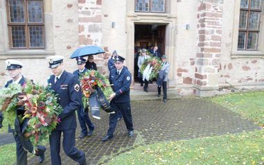 Männer in Uniformen, die mit Kränzen aus der Phillip-Nicolai Kirche gehen.