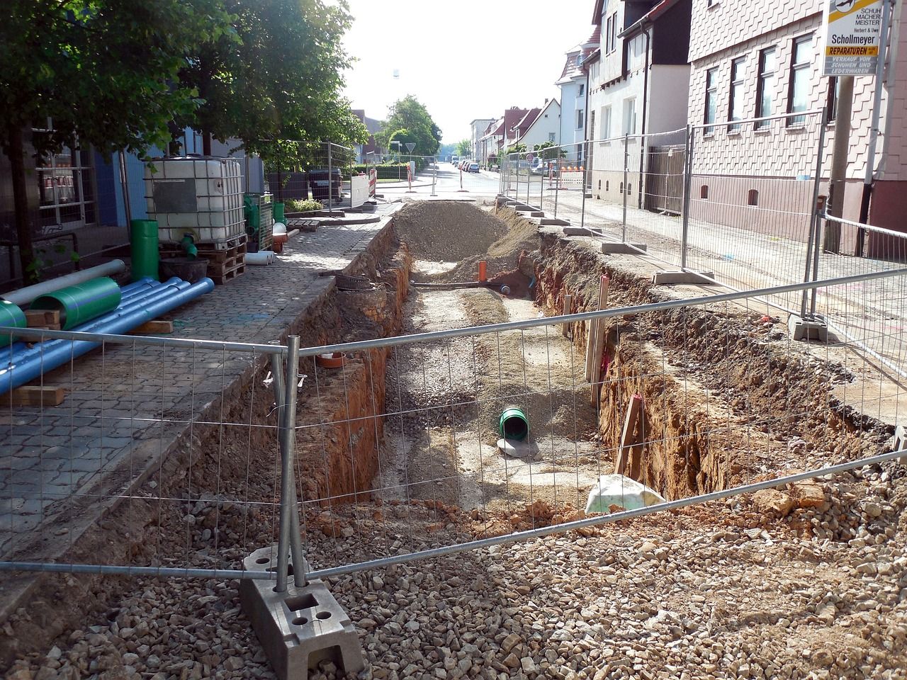 Ein tiefer Graben auf einer abgezäunten Baustelle in einer Stadt.