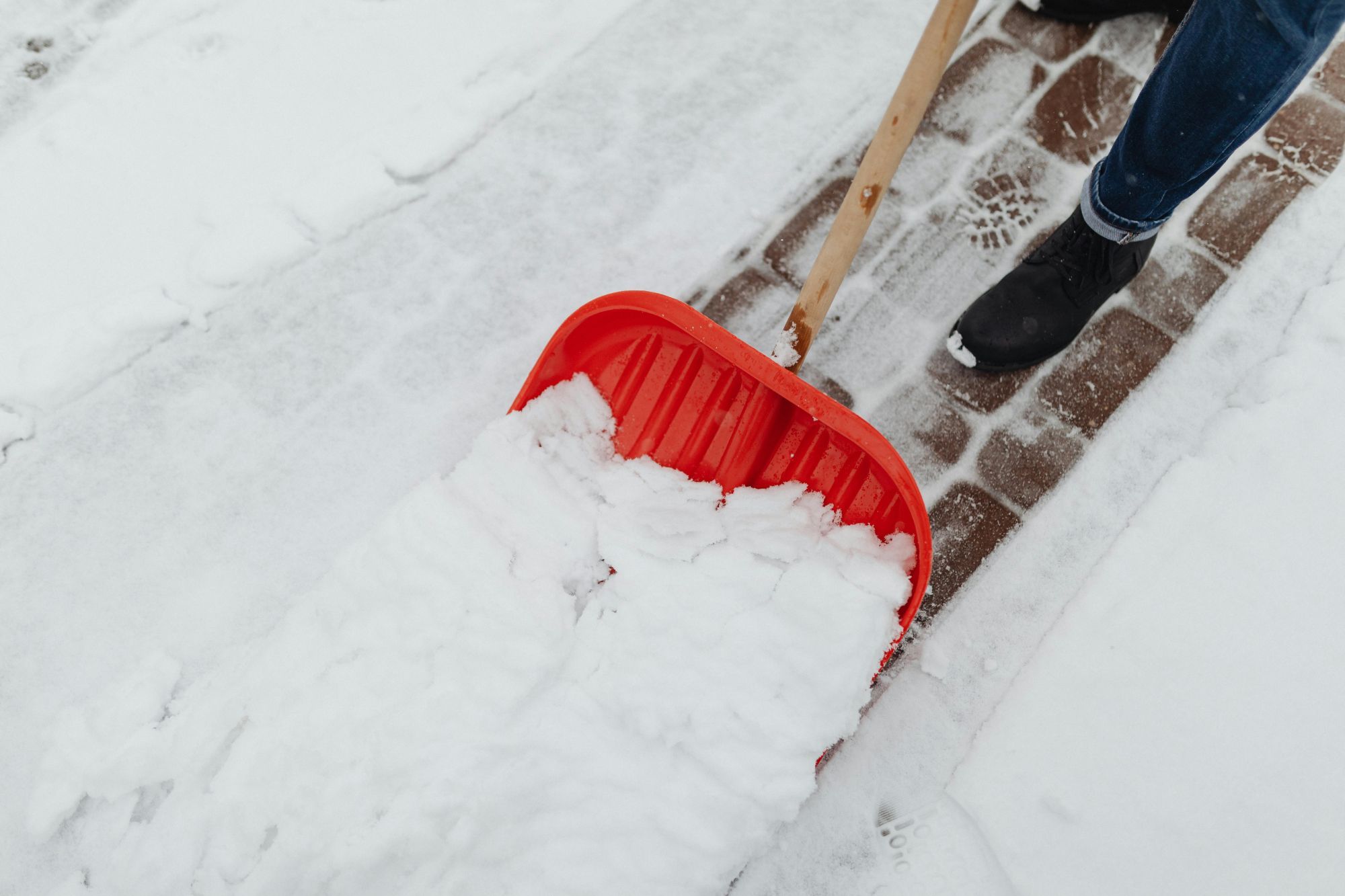 Eine Person die mit einer roten Schaufel Massen an Schnee von einem Gehweg schiebt.