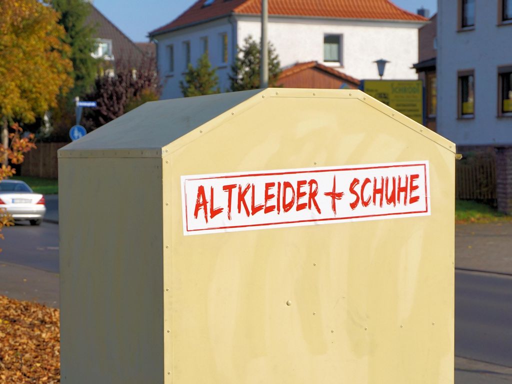 Ein Altkleidercontainer mit der Aufschrift Altkleider + Schuhe, der an einer Straße steht.