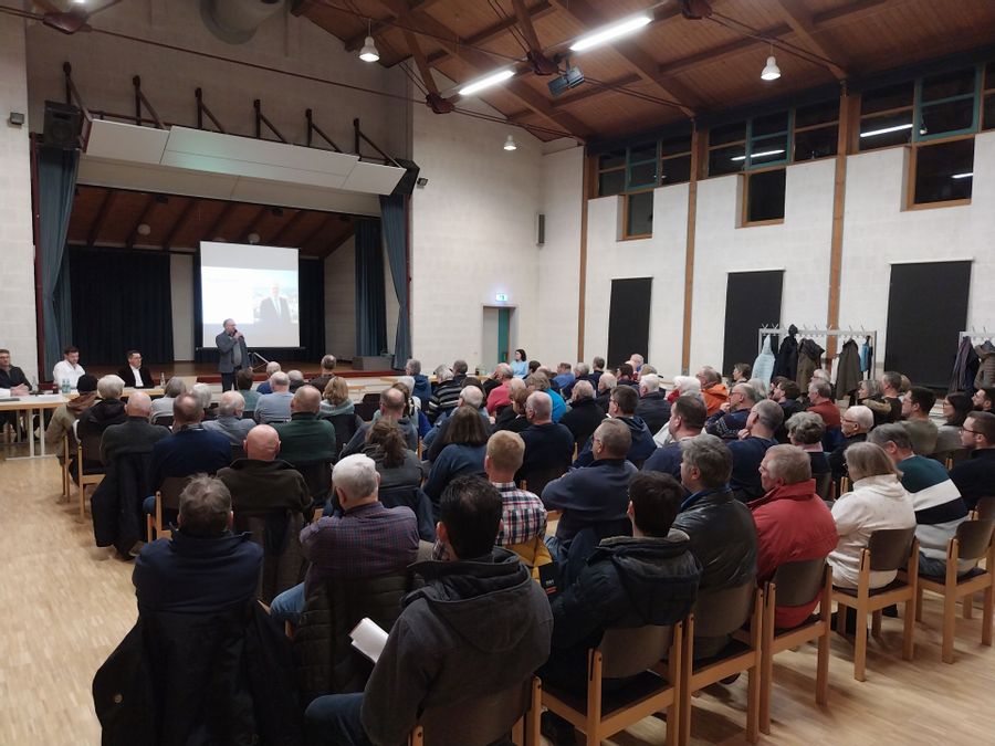 Vielen Menschen sitzen in einem Saal, um einem Redner zu lauschen.