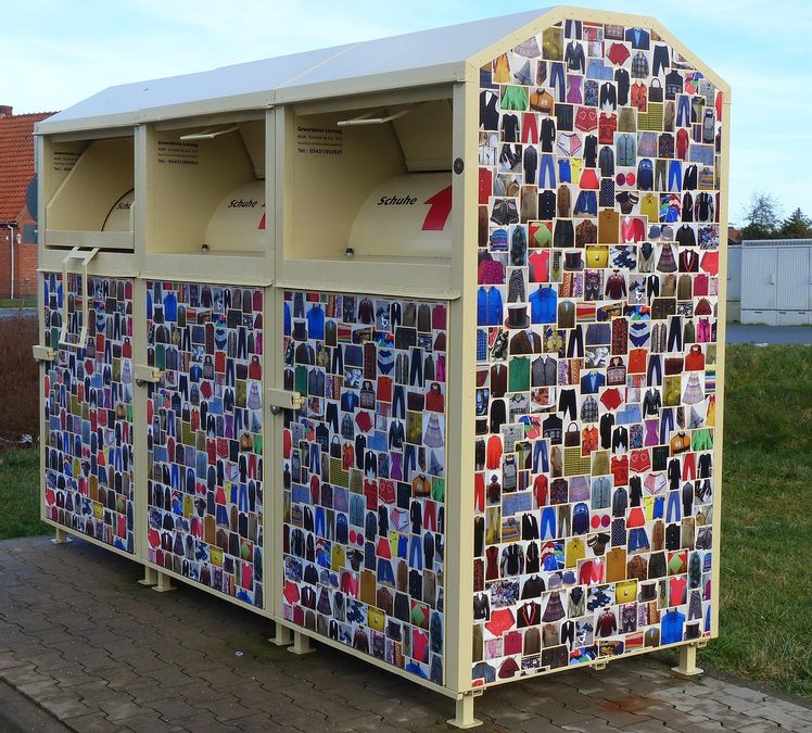 Drei Container für Altkleider steht auf einem Weg.