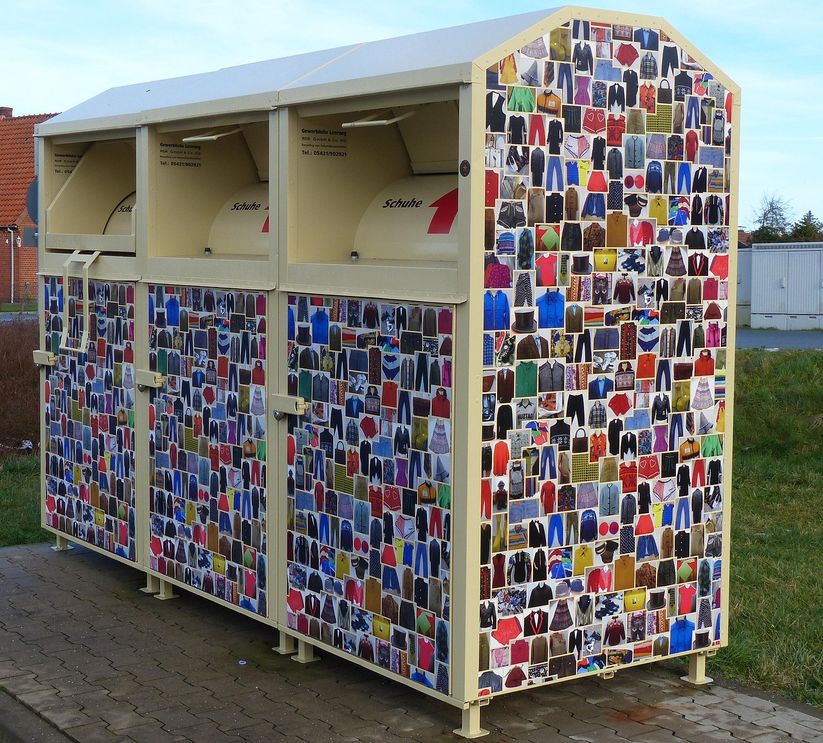 Drei Container für Altkleider steht auf einem Weg.
