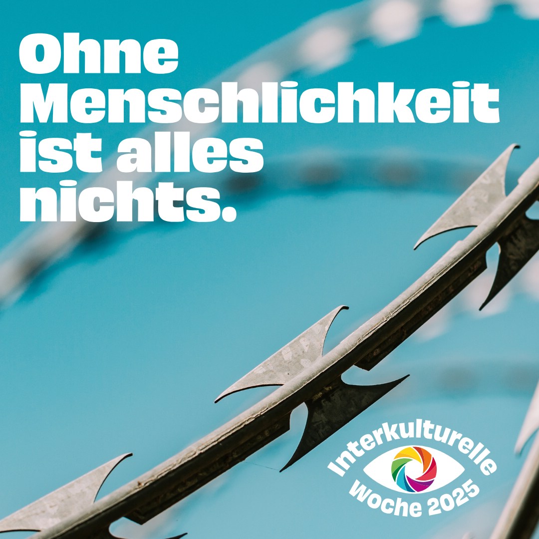 Es ist ein kleiner Teil es Metallzaunes zu sehen. Blauer Hintergrund und der Text Ohne Menschlichkeit ist alles nichts. Unten rechts ist das Logo Interkulturelle Woche 2025 zu sehen.