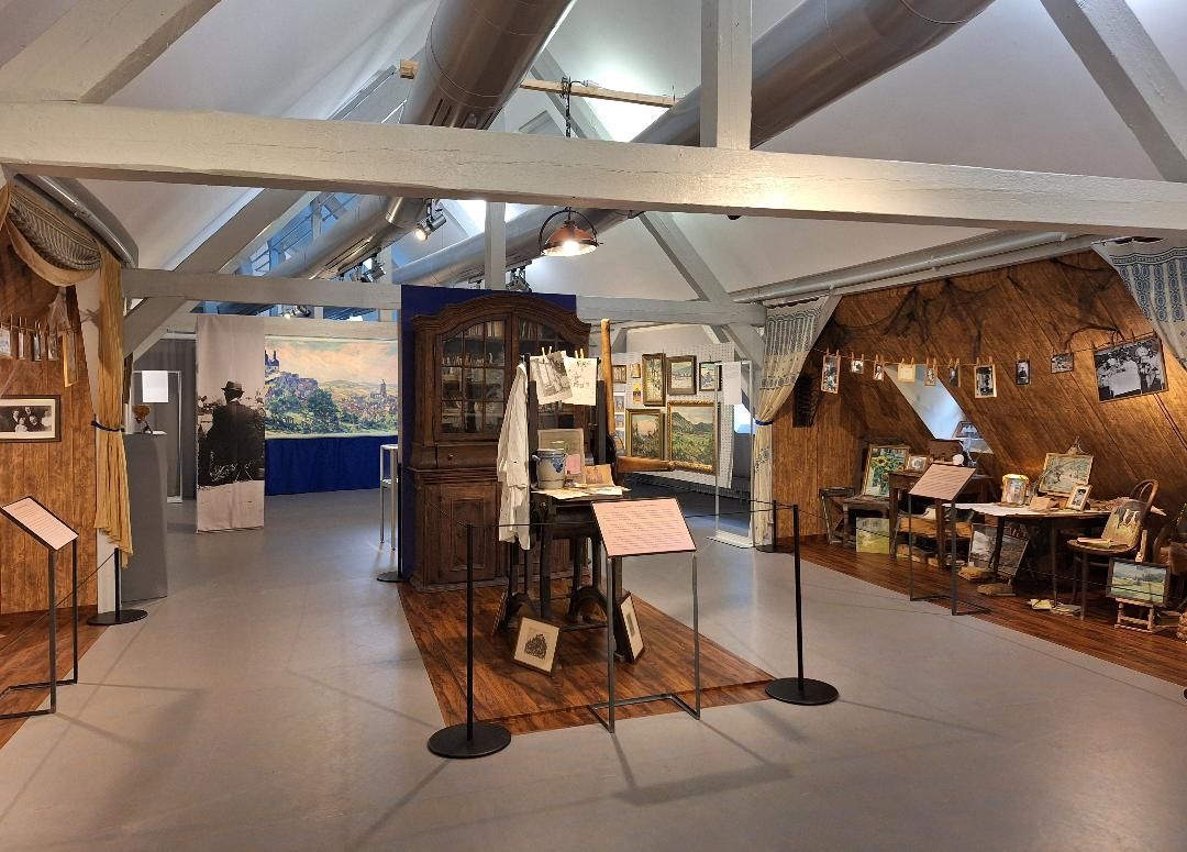 Auf dem Bild ist ein Teil der neuen Dauerausstellung von Willi Tillmans zu sehen: Einige seiner Werke sowie ein Teil seines Ateliers mit Tisch, Stühlen, Schrank und aufgehängten Bildern.