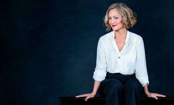 Zu sehen ist die Pianistin Anne Folger auf einem Klavier sitzend mit weißer Bluse und schwarzer Hose.