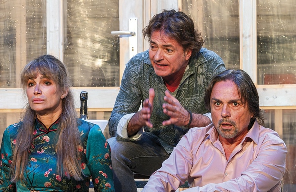 Zu sehen sind eine Frau und zwei Männer, die sitzen und aufgebracht wirken.